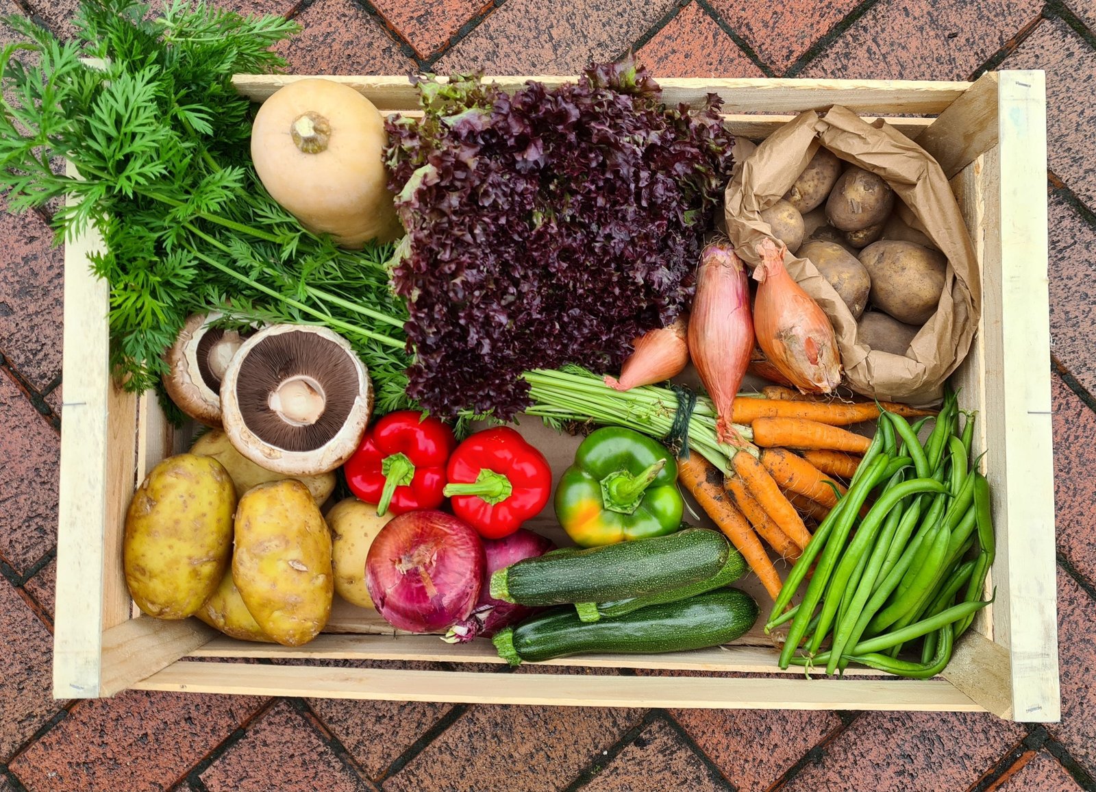 A packed summer veg box crate on the brick paving